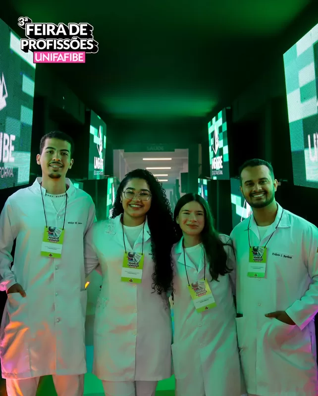 Grupo de estudantes da UNIFAFIBE na Feira de Profissões. Jovens sorrindo, vestindo jalecos brancos e crachás do evento.