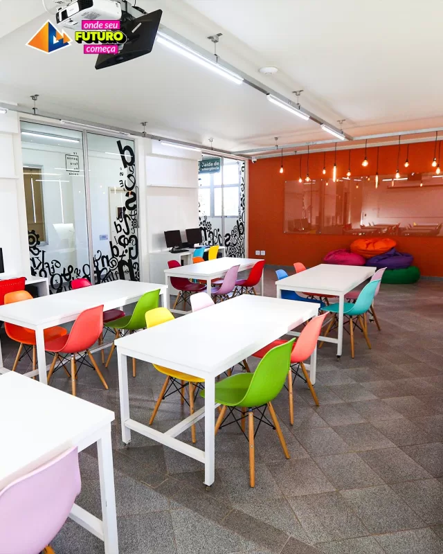 Interior da UNIFAFIBE: mesas brancas com cadeiras coloridas, iluminação moderna e pufes. Espaço de aprendizado vibrante e inovador.